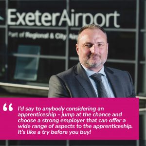 A picture of the managing director of Exeter Airport, Stephen Wiltshire. He is wearing a suit and tie. He is stood in front of the Exeter Airport sign.